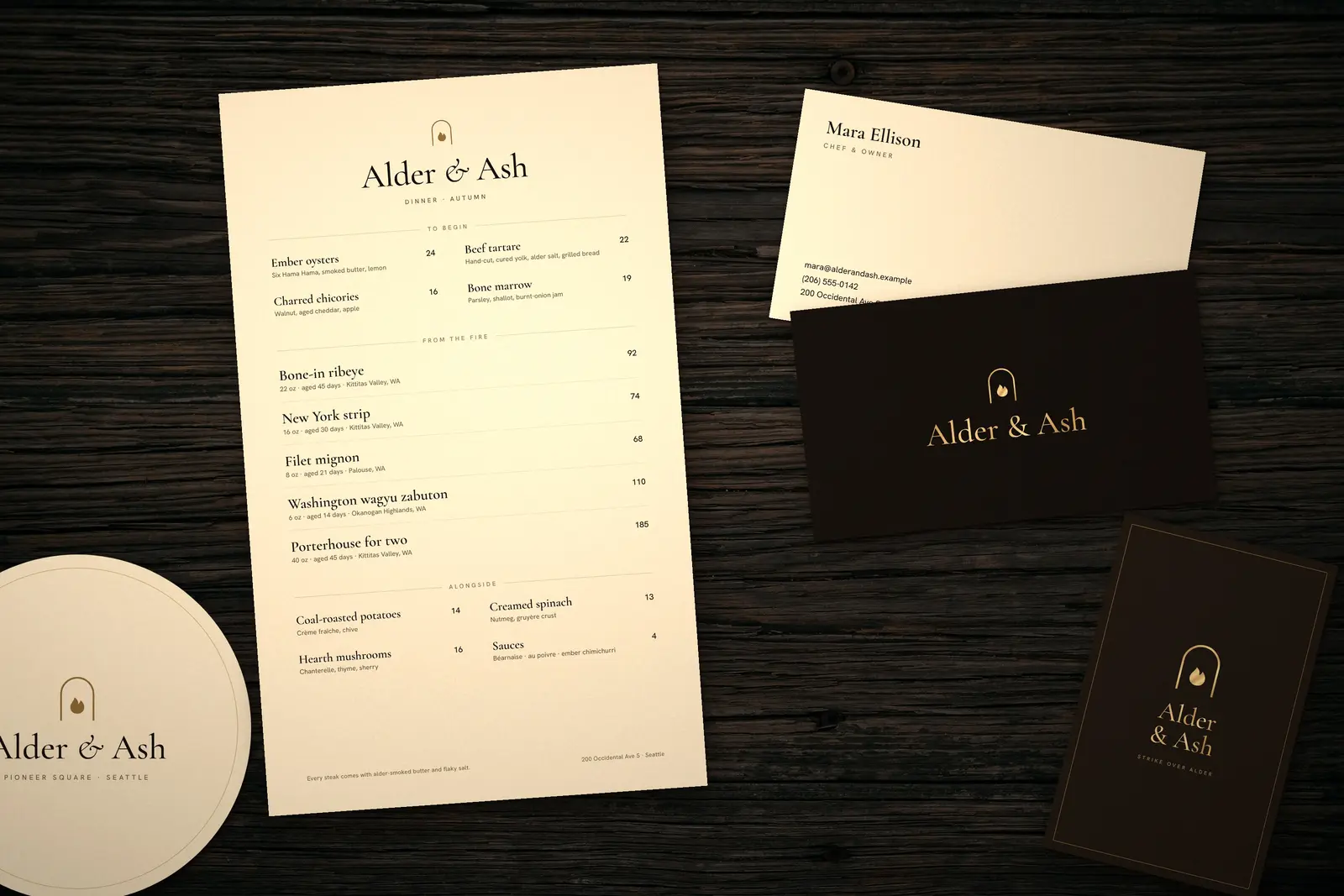 Alder & Ash menu, business cards, matchbox and coaster on a dark wood table